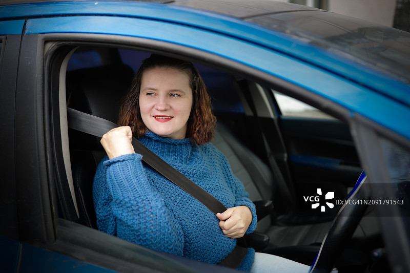 穿着毛衣的加大码中年妇女在右舵汽车上系安全带图片素材