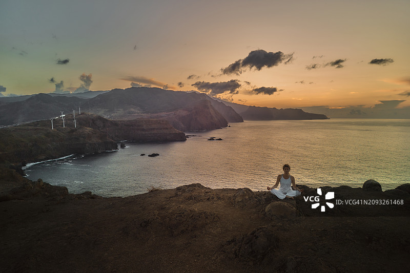 在日落时分的海上山顶冥想的放松的运动型女人图片素材