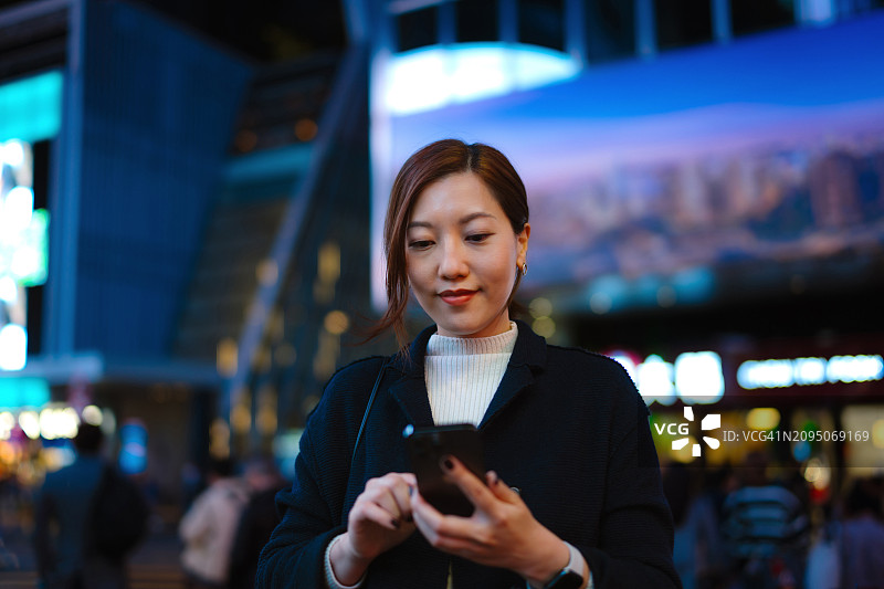 夜晚城市里使用智能手机的亚洲年轻女子图片素材