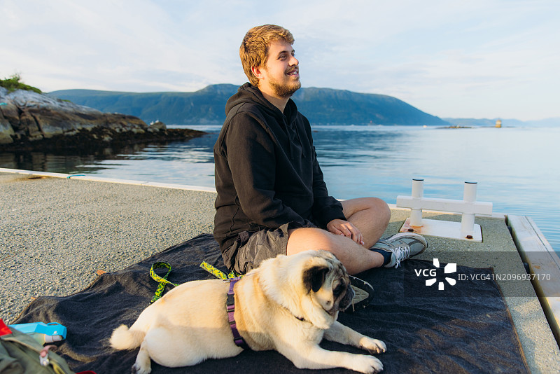快乐的男人和狗在挪威海边欣赏夏日山景图片素材