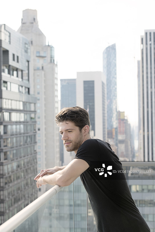年轻男子倚靠在纽约市的阳台上图片素材