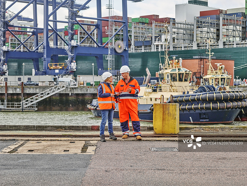 码头工人在拖船和集装箱船前手持平板电脑站立图片素材