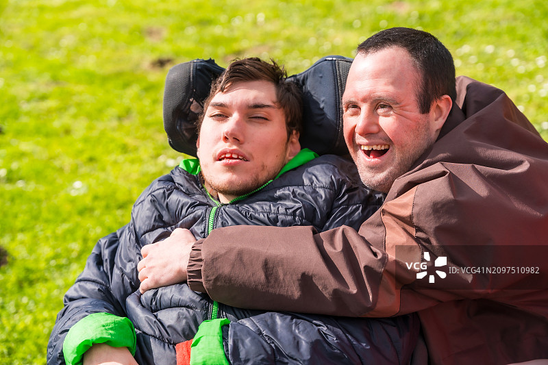 患有唐氏综合症的男人在公园里拥抱患有脑瘫的男人图片素材