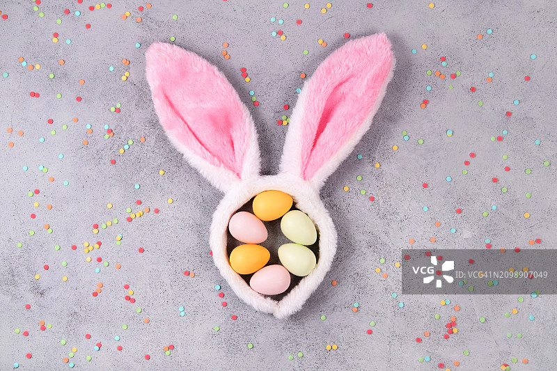 可爱的兔子耳朵，里面有彩色复活节彩蛋和五彩纸屑在水泥背景上图片素材