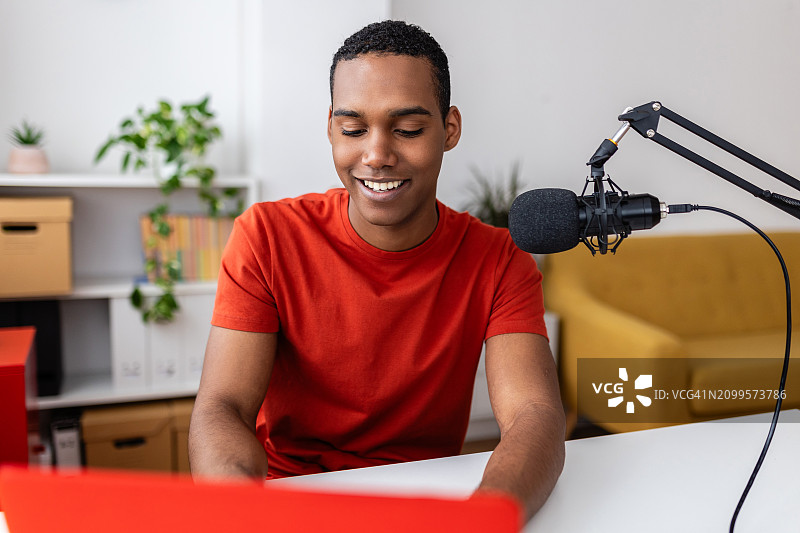 快乐的年轻男学生在家里的工作室用笔记本电脑录制播客图片素材