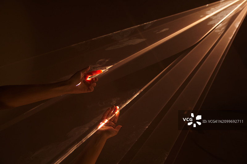 不同人的两只手伸向黑暗背景中激光束的黄色光芒。新生命的概念，带有复制空间。图片素材