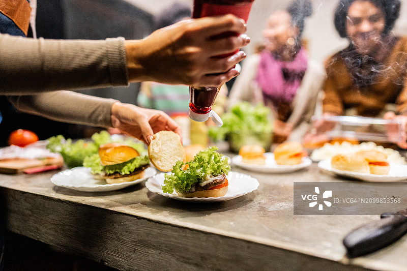 女人晚上在家和朋友一起在汉堡上放番茄酱的特写图片素材