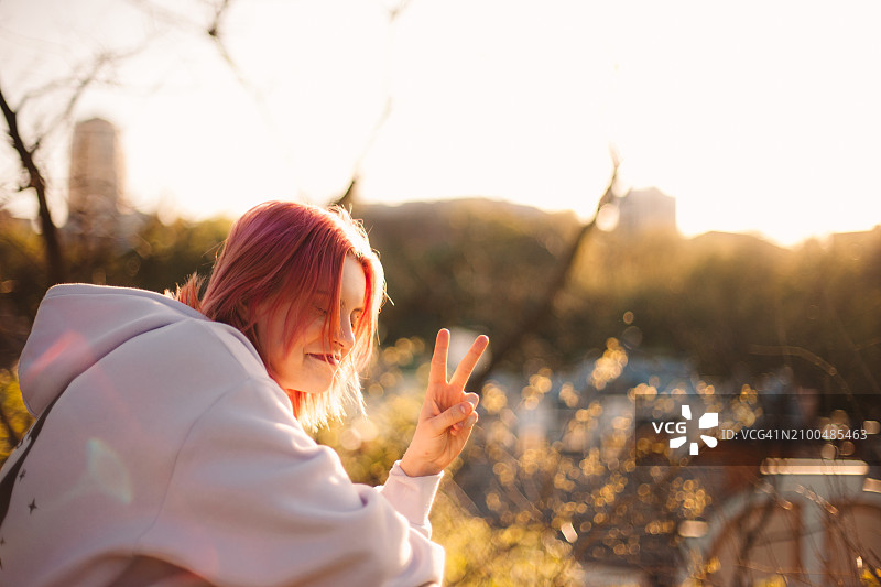 快乐的年轻女人在春天的公园里做出和平手势图片素材