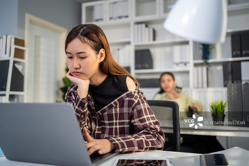 在办公室加班感到沮丧的亚洲女商人，坐在办公桌前，因使用笔记本电脑工作而感到压力和失望图片素材