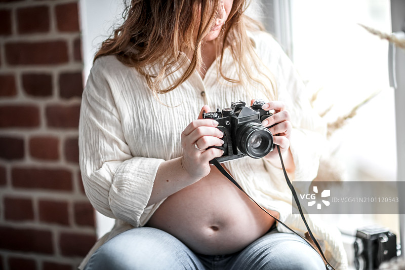 孕妇坐在窗台上用复古相机捕捉的反思时刻图片素材