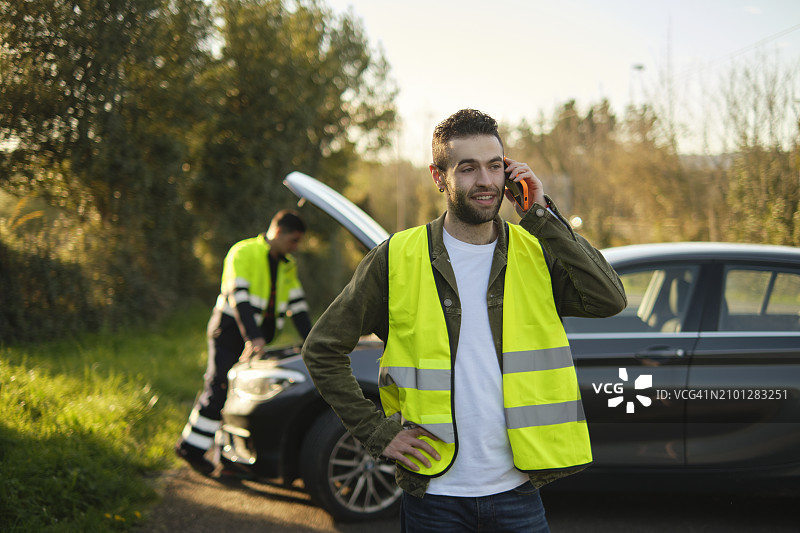 男子在路边打电话，同时修理工检查他损坏的汽车图片素材