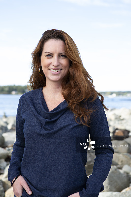 在多岩石海边微笑的长发中年女人图片素材