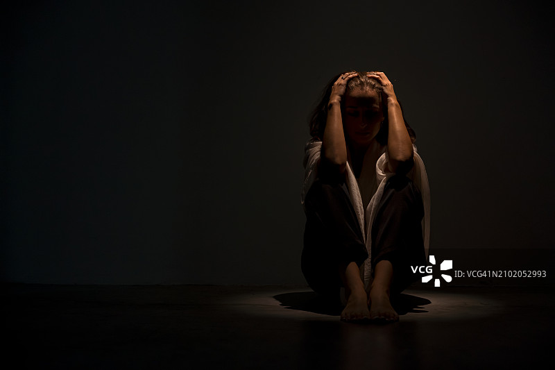 焦虑的女人坐在地上抱着膝盖，感到害怕，抑郁和心理健康问题图片素材