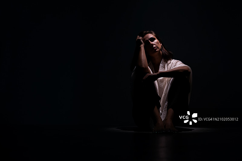 焦虑的女人坐在地上抱着膝盖，感到害怕，抑郁和心理健康问题图片素材