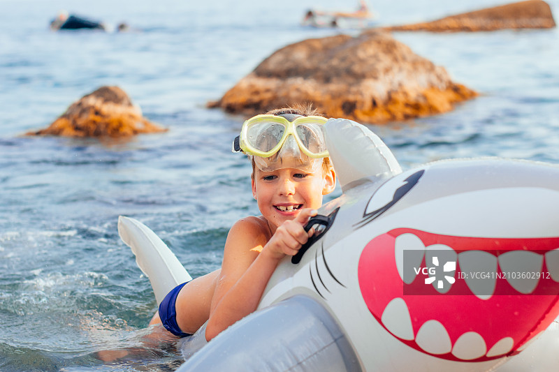 快乐微笑的男孩在海里与充气鲨鱼玩耍图片素材