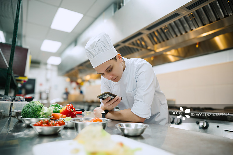 亚洲厨师在厨房休息期间使用手机图片素材