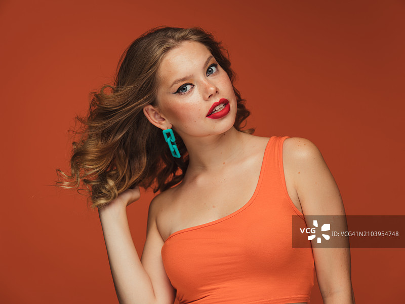 橙色背景上，化着鲜艳妆容、涂着红色口红的橙色上衣女子图片素材