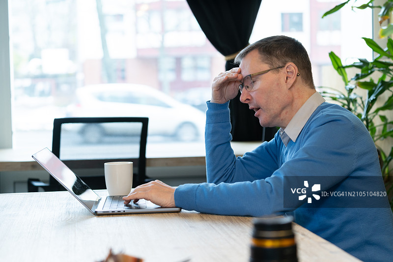 戴眼镜的男人在办公室工作时看起来疲惫或痛苦图片素材