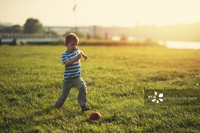 在美丽的草地上踢足球的可爱小男孩图片素材
