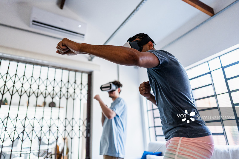 年轻男人在家与朋友一起使用VR眼镜图片素材