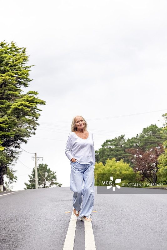 晴天里，年长的女人在路上行走，背景留白图片素材