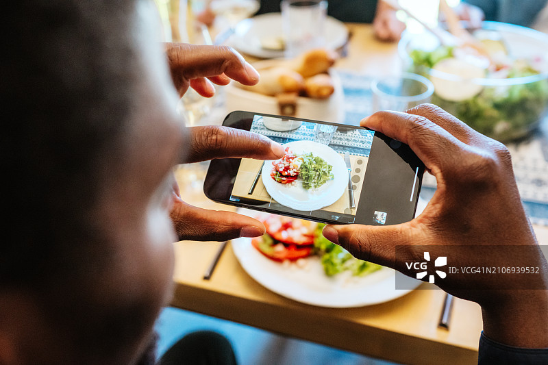 晚餐时用智能手机拍摄食物照片的人图片素材