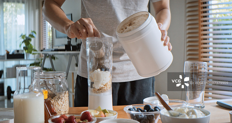 年轻亚裔男子用搅拌机准备蛋白奶昔，混合水果谷物汁图片素材