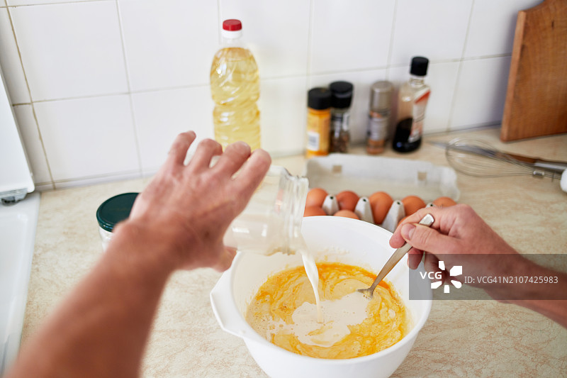 男人将牛奶倒入自制煎饼的面团中，自制食品烹饪概念图片素材