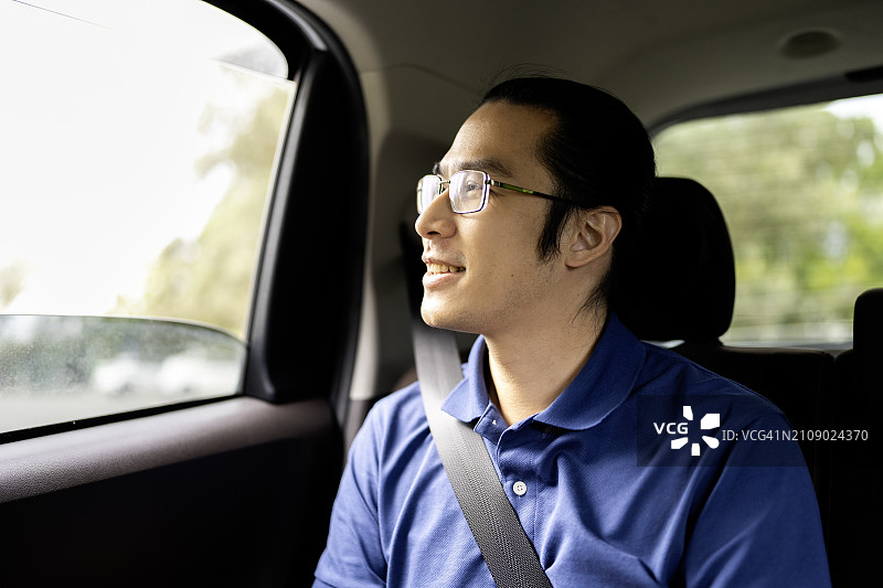 坐在汽车后座，微笑并向窗外看的亚洲男人图片素材