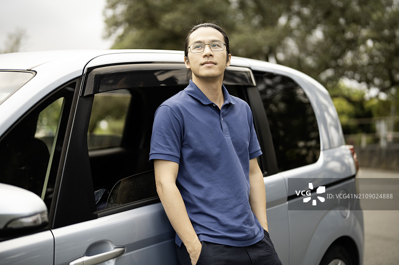 手插口袋靠在车门上，眺望远方的亚洲男人图片素材