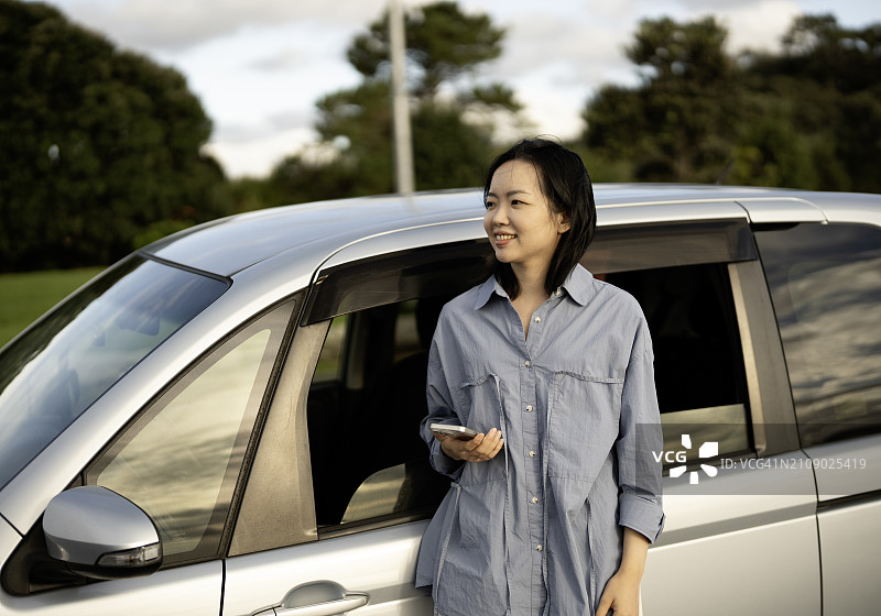 亚洲女性靠在车门上手持智能手机凝视远方图片素材