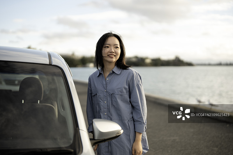 准备上车的亚洲女人：车停在防波堤上，太阳即将落山图片素材