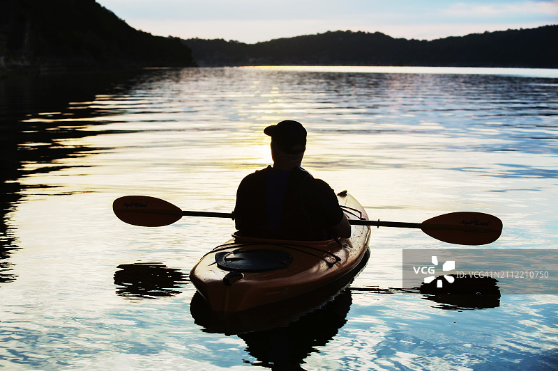 日出时在湖上划皮划艇的男人剪影图片素材