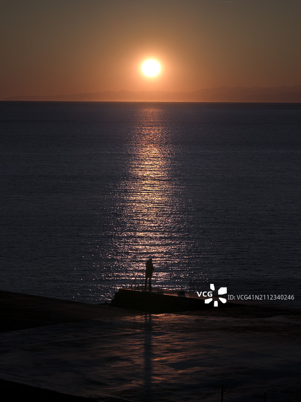 日落时分，男子在海上乘船的轮廓图片素材