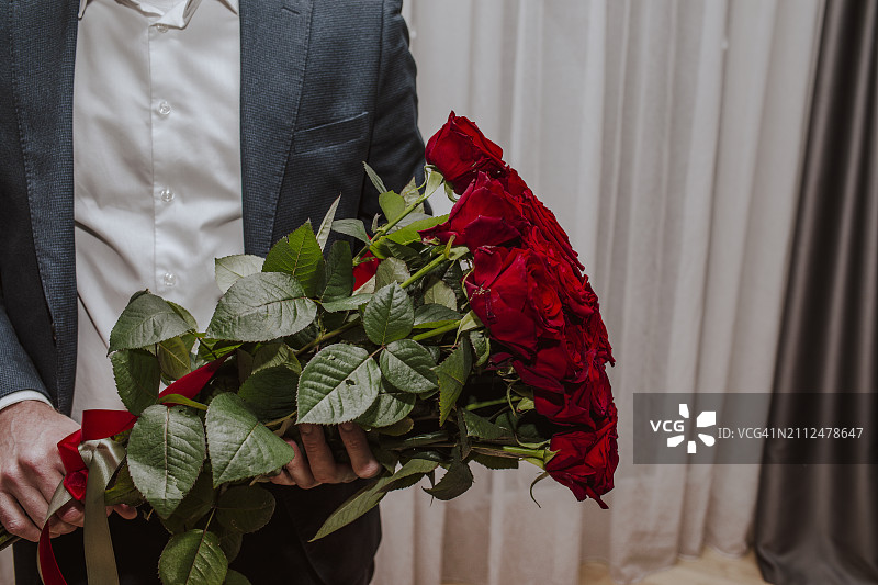 穿着西装，在家手捧红玫瑰花束的男孩图片素材