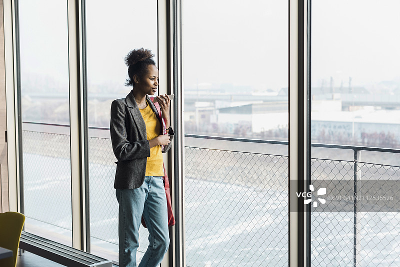 年轻女商人拿着手机在办公室望着窗外图片素材