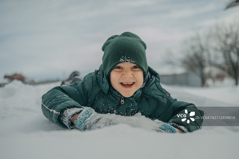 快乐的男孩躺在雪地上玩耍图片素材