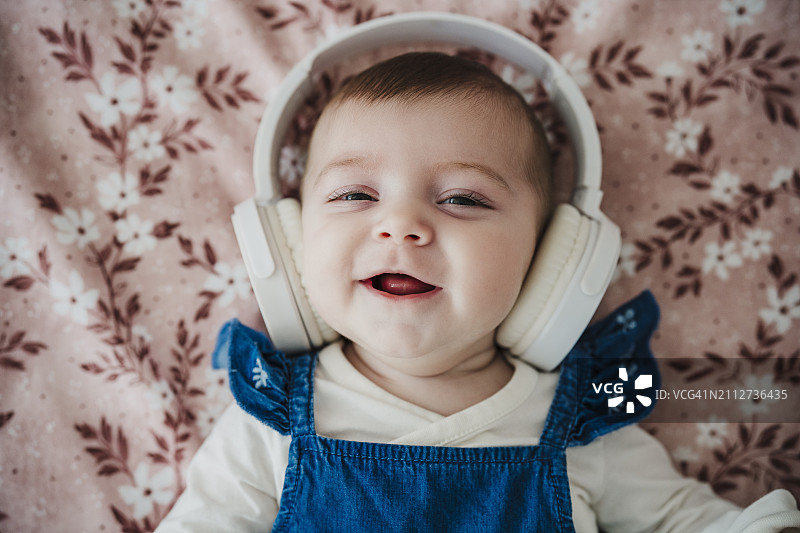 戴着无线耳机躺在床上的可爱女婴图片素材