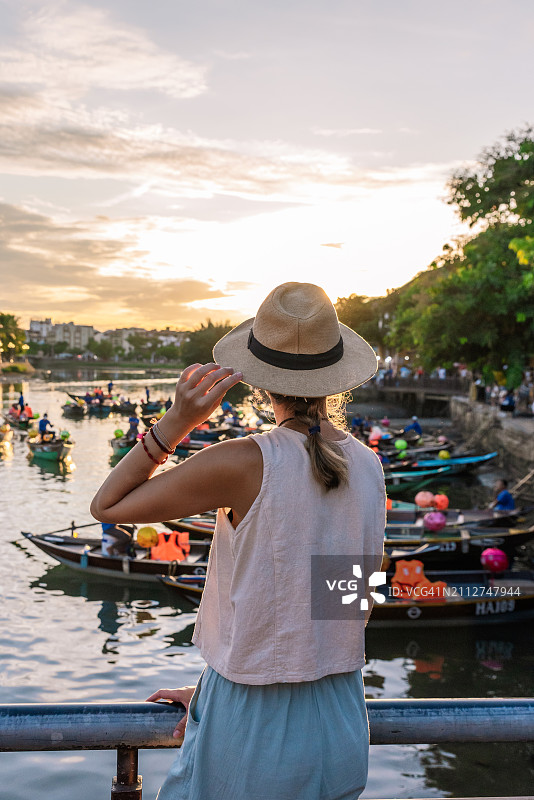 戴帽子的年轻女人欣赏日落时分满是船只的秋盆河图片素材