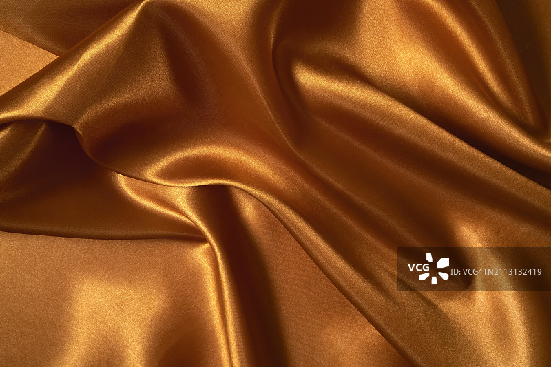 带有波浪和褶皱的金色棕色缎面纹理背景，用于奢华产品展示的黄色布料背景，平铺，特写图片素材