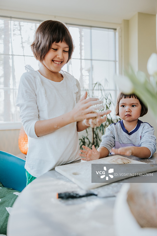 两个快乐的姐妹坐在厨房的桌子旁，一起揉捏甜糕点的面团图片素材