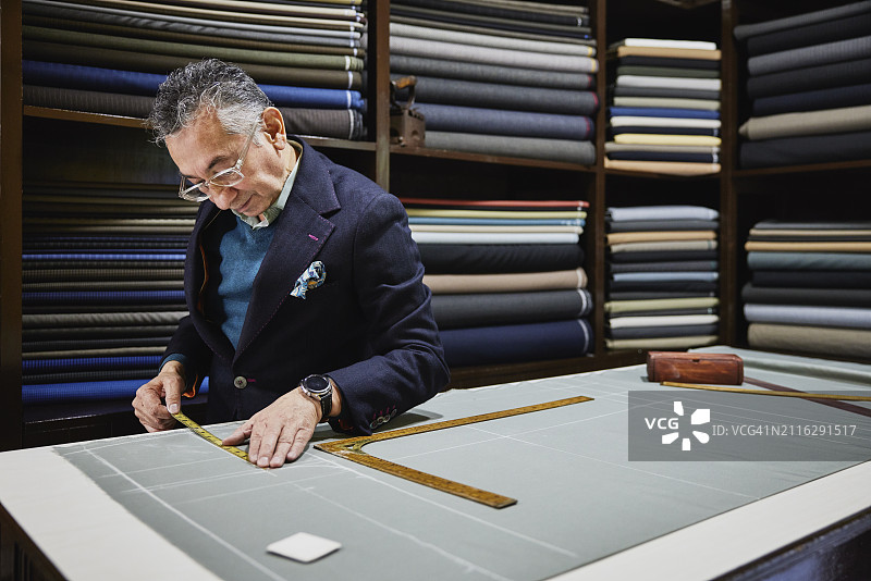 裁缝在工作室的桌子上测量西装面料图片素材