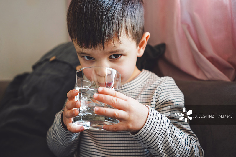 可爱的小男孩用透明玻璃杯喝水特写肖像图片素材