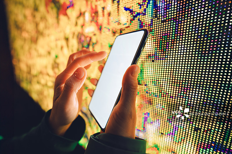 城市互联：手持智能手机与彩色LED屏幕背景图片素材