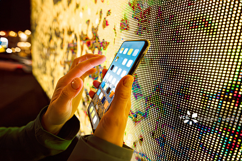 城市互联：手持智能手机与彩色LED屏幕背景图片素材