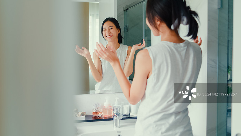 年轻亚洲女性在家中浴室玩得开心，涂抹面霜并照镜子。居家日常图片素材