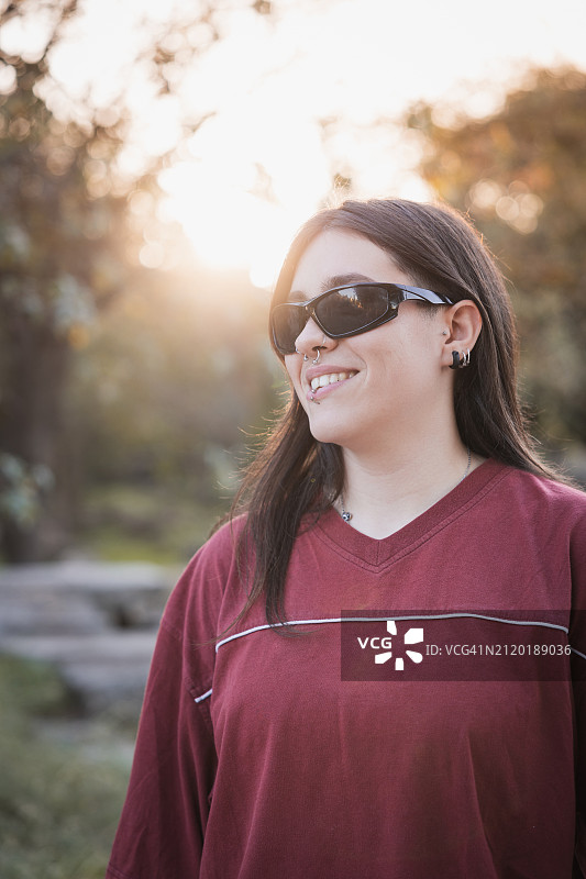 快乐的年轻女子在公园宁静的环境中戴着耳环和太阳镜图片素材