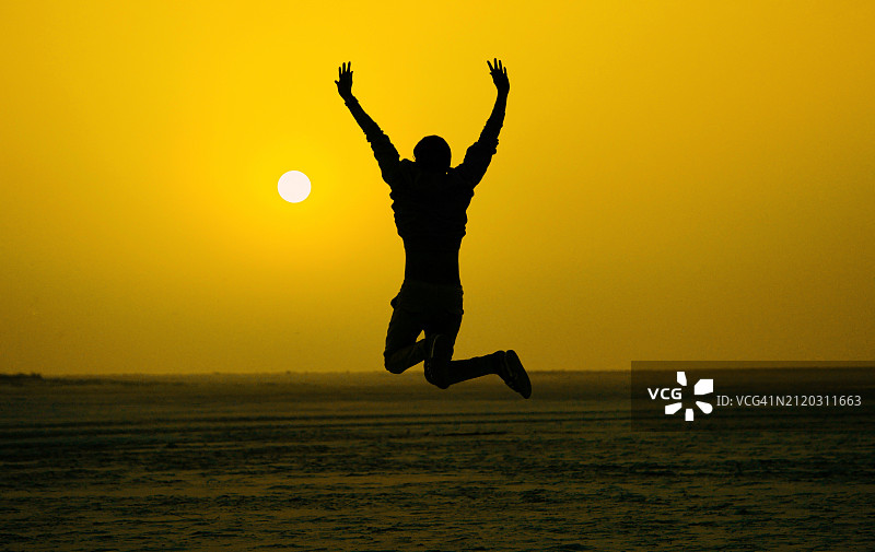 日落时分，男子在孟加拉国邦昂联盟海滩跳跃的剪影图片素材