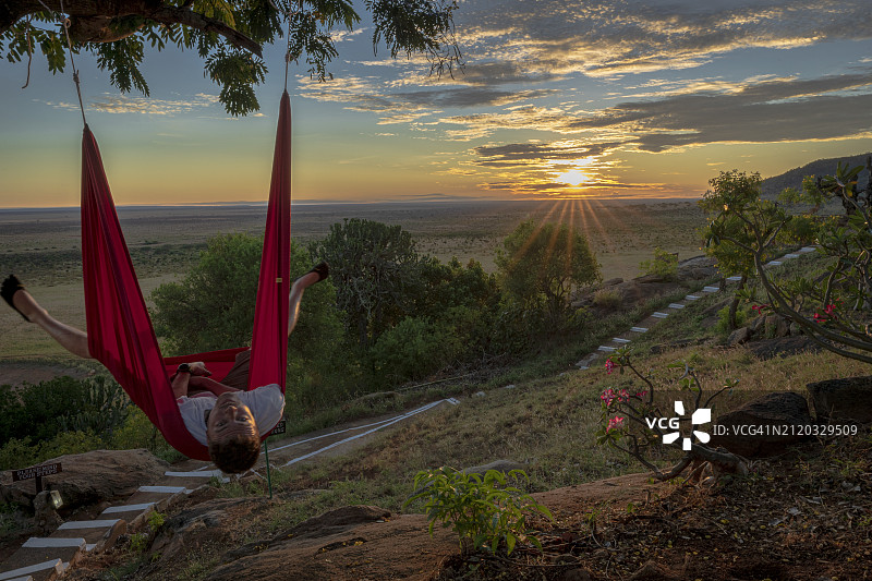 日出时分，男子在肯尼亚马赛马拉动物园的粉色吊床上休息图片素材