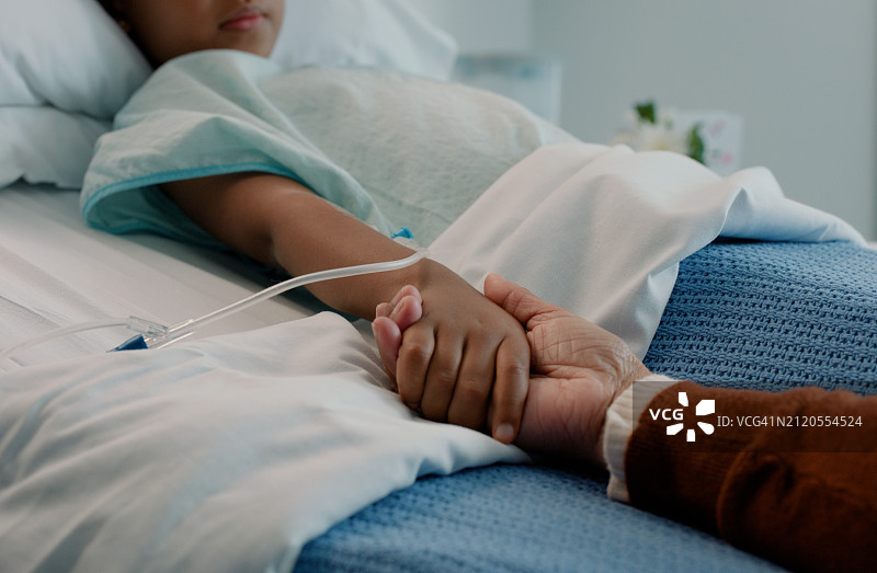 医院：术后儿童在病床上被握手，在诊所中获得关爱与支持图片素材